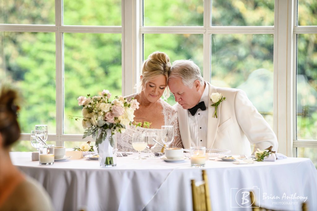 Bride and Groom pause for a blessing before the wedding reception dinner. The are seated together at the "sweetheart table" with their heads touching during the blessing.